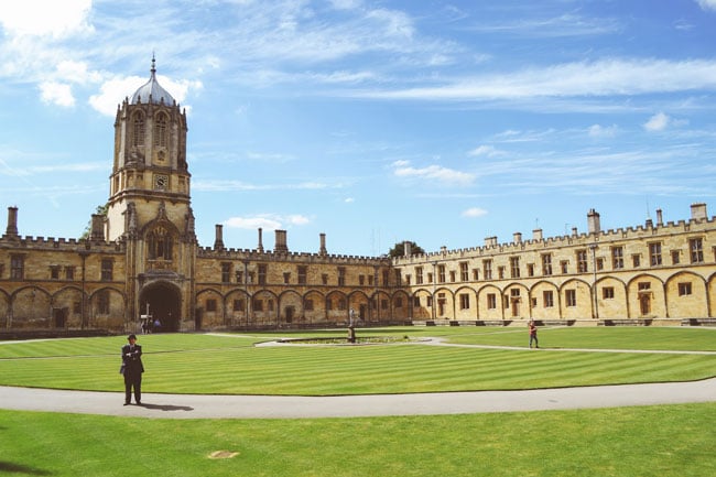 A large green lawn grows in a courtyard surrounded by old buildings