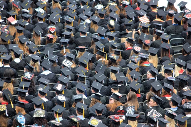 A crowd of graduates wearing hats and robes all sit together