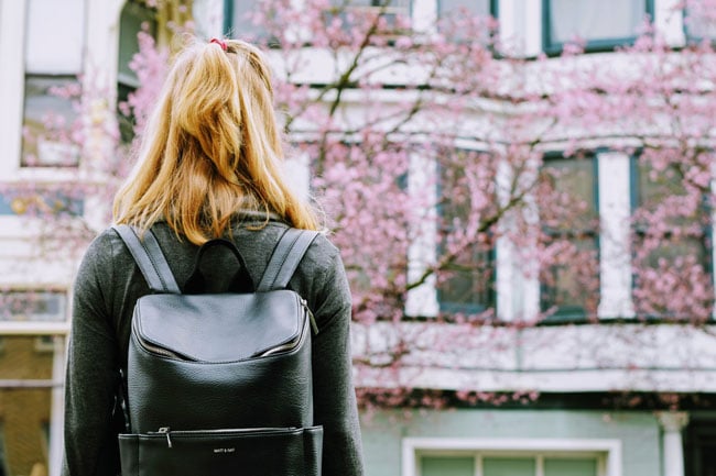 A student wearing a backpack faces a pink blooming tree in front of a building
