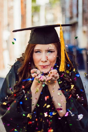 a graduate blows confetti