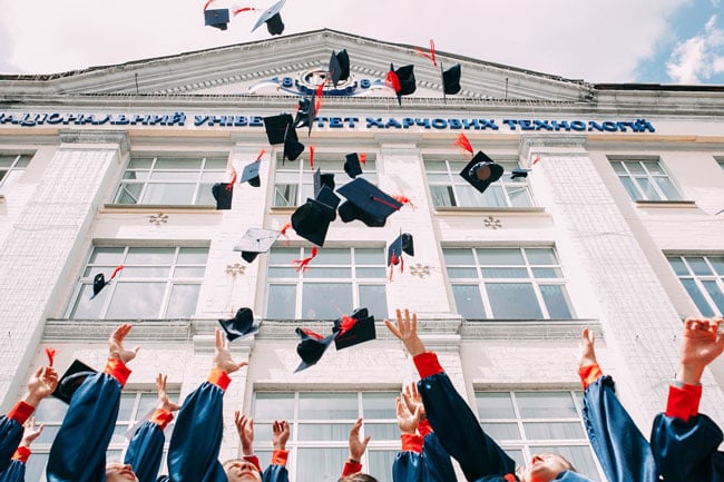 Students raise their hands and toss their graduation caps into the air