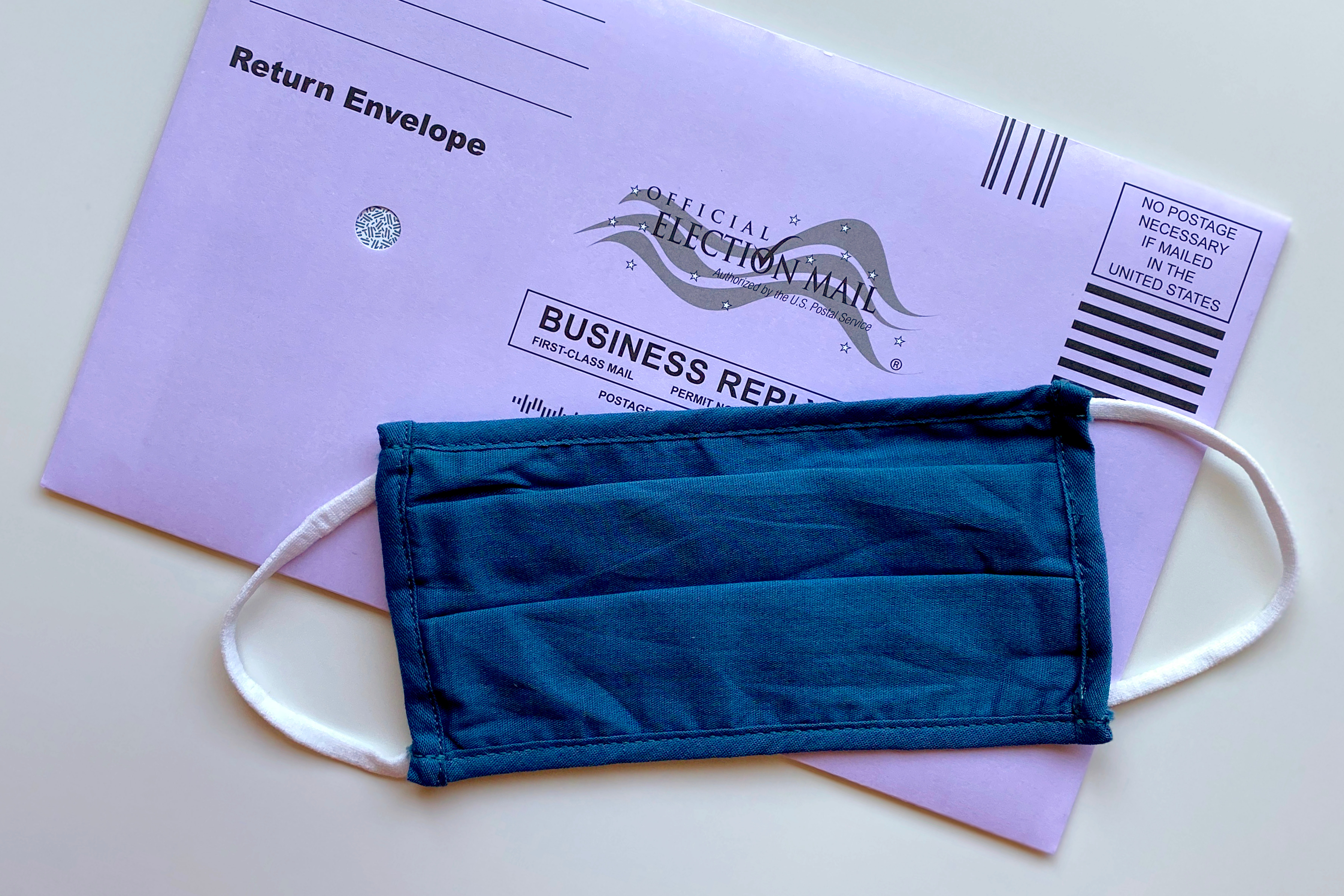 a purple mail-in ballot envelope and a blue face mask