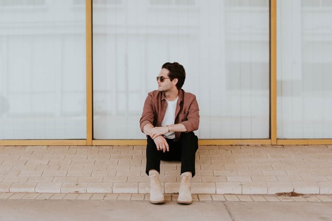 man sits and waits on the sidewalk