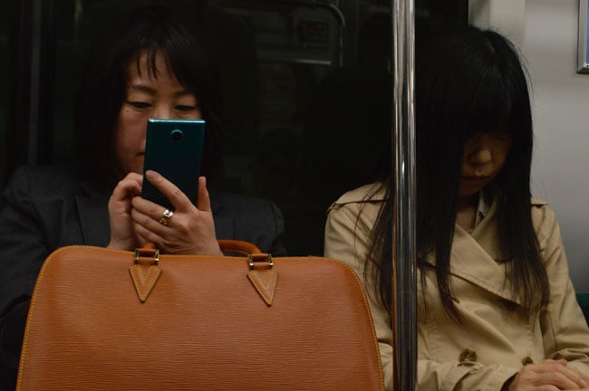 woman on train with beige bag looking at her phone next to another woman