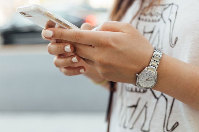 woman with white fingernails and watch holding a phone